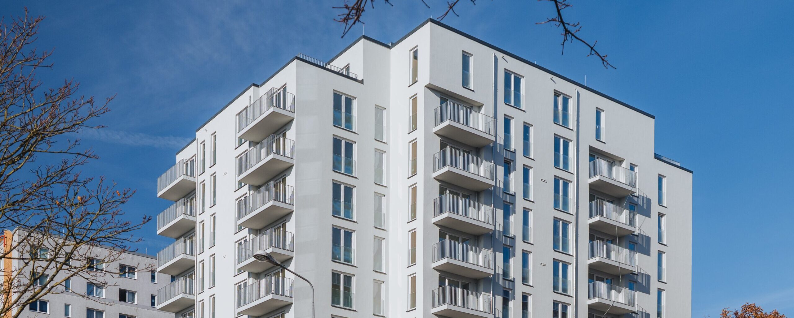 ein weißes Hochhaus vor blauem Himmel mit Balkonen und vielen bodentiefen Fenstern, Warnowallee 23a in Rostock Lütten Klein